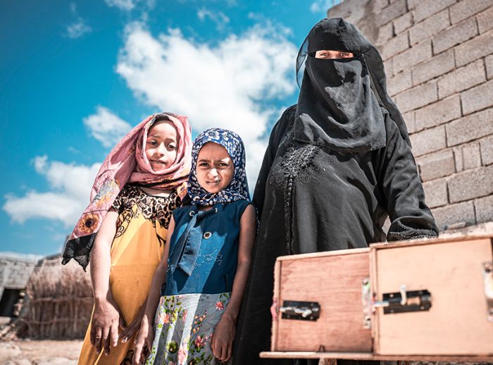 Nazrah and her children standing beside beehive