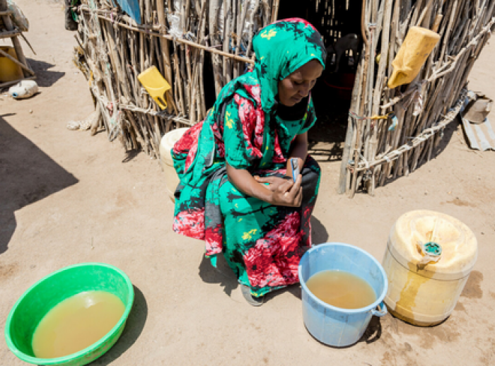 Safia adding purification treatment to bucket of water.