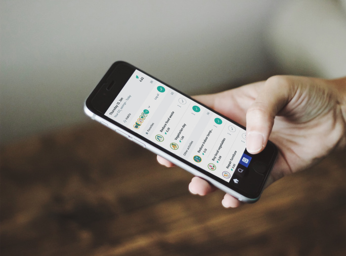 A hand holding a mobile phone, navigating on Oxfam's Corporate Sustainability challenge app interface