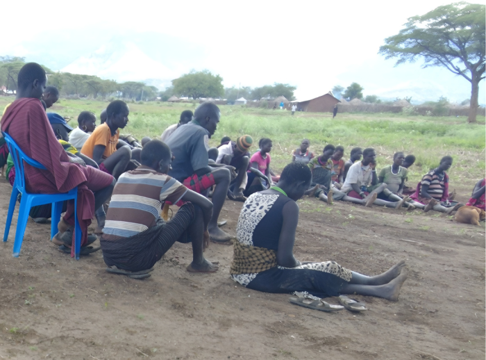 Group of people sitting in semi circle on the floor during a Farmer field schools lesson