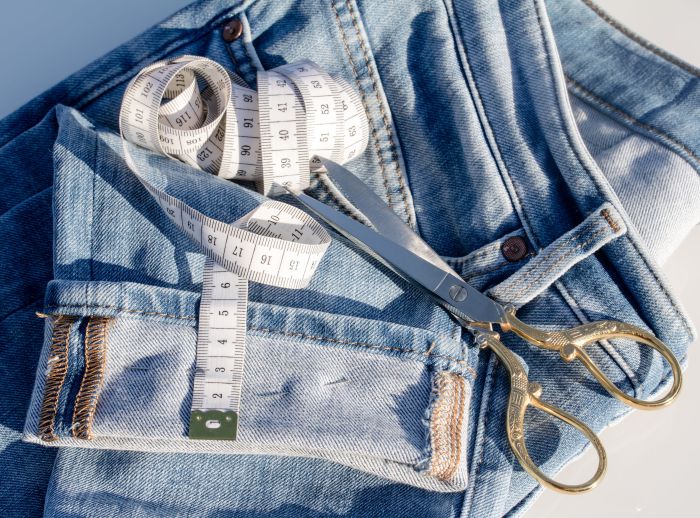 A pair of Jeans set to be amended. There is sewing scissors and measuring tape on top of it.