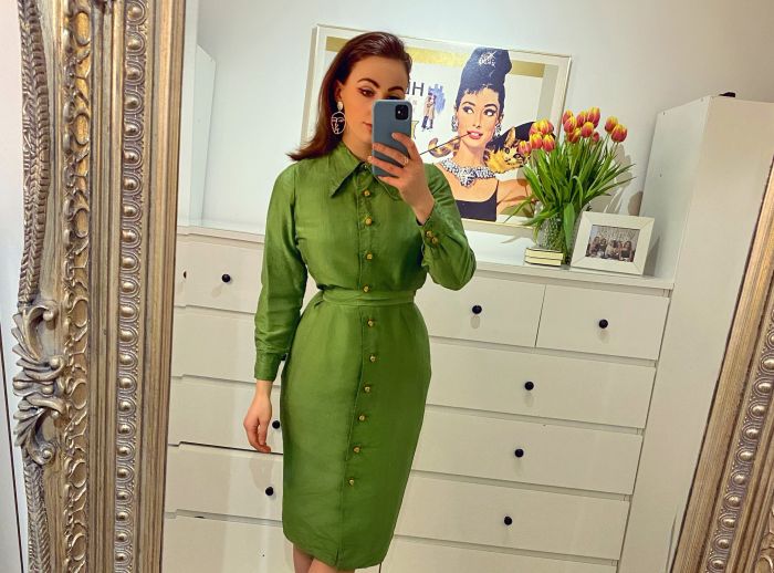 Fiona pausing in front of a mirror taking a selfie of her second hand green dress