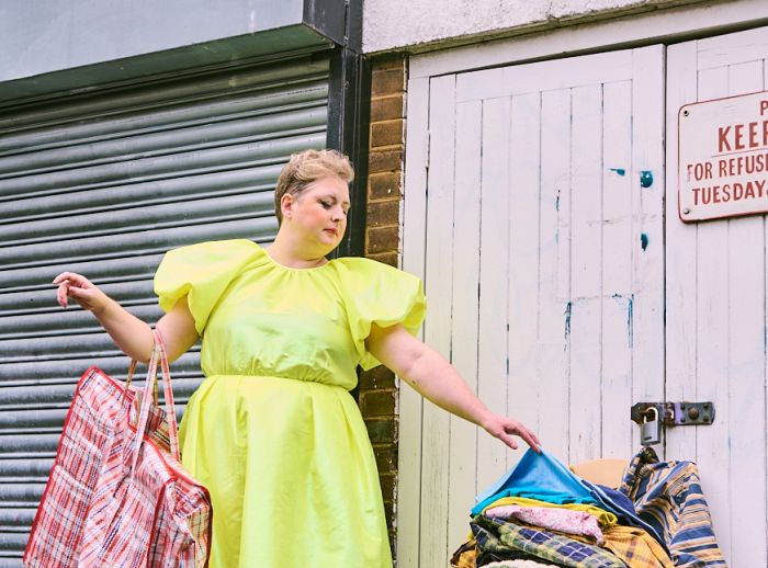 Siobhan McSweeney holding a big shopping bag while looking at second hand clothes on a chair.