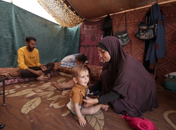 Duaa Abu Sabha is dressing her child in clothes inside her tent in the Al-Mawasi area of Khan Yunis Governorate. Her other children and husband are in the background.