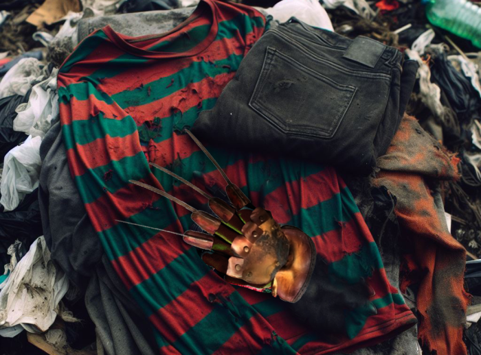 Image of Freddy Krueger Halloween outfit on top of a pile of clothes in the landfill.AI generated content.