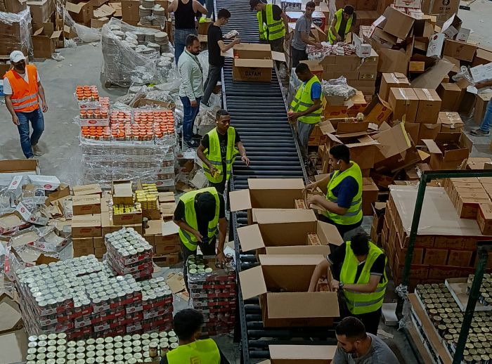 Loading and packing a shipment of dry food parcels from Oxfam that was prepared for delivery. there is over 20 people packing food parcels and sorted all the boxes in a warehouse type location..