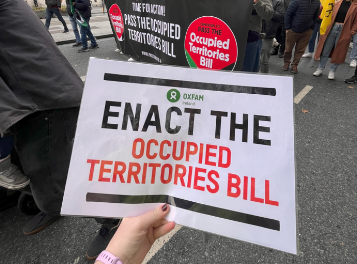 Person holding a poster with "Enact the Occupied territories bill" and the Oxfam Ireland logo during the nationwide demonstration
