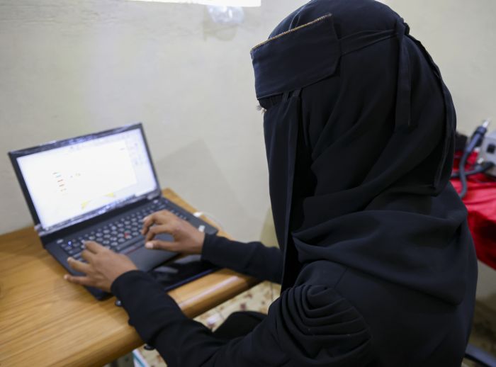 Nahla Abdo sits at a wooden desk, working on a laptop with electronic tools nearby.