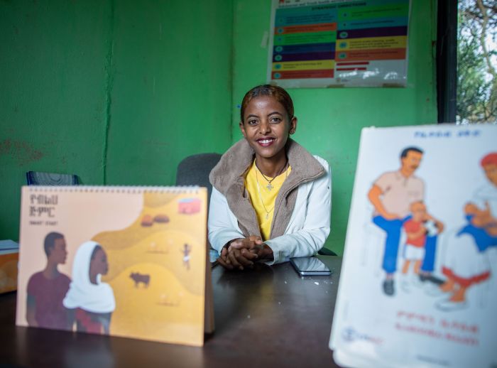 Bethlehem "Betty" Feleke, a nurse, smiles at the camera from her desk in a clinic, with informational booklets in the foreground.