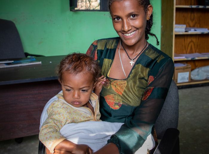 Atsede Bere smiles at the camera while holding her child in a clinic.