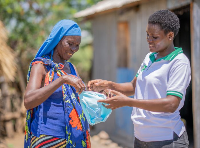 Patricia Lotieng, WASH Coordinator at TUPADO, hands a sanitary kit to Margaret Ekamai, program participant.