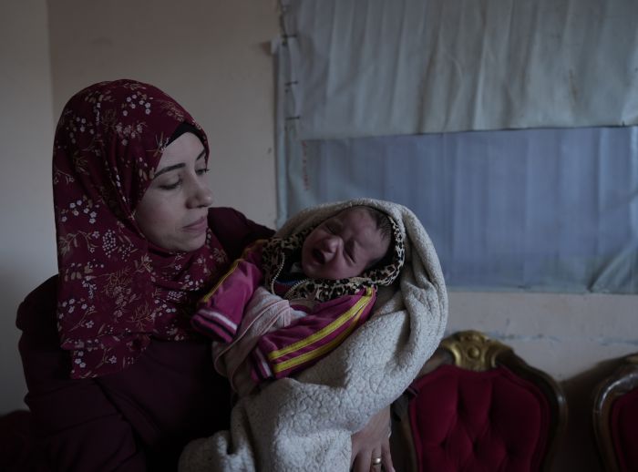 Suhad holds her child in a room with red chairs and a curtained window