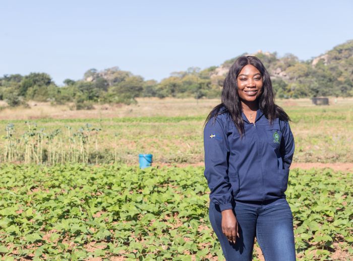 Nicole Mubikah stands in a lush green field in Zimbabwe, where she works with smallholder farmers facing the harsh realities of climate injustice.