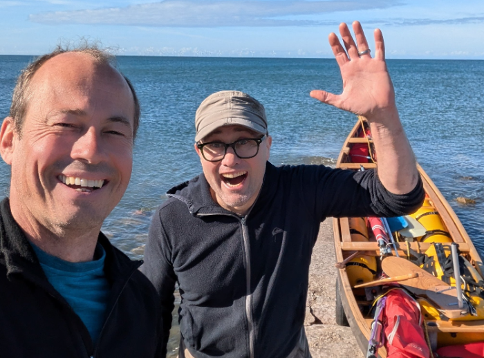 Johan Hoving smiling on the left and Rich Ensoll waves on the right beside their canoe.