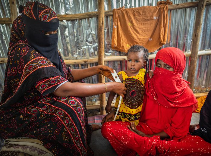 Fatuma Humad measures two-year-old Aradi’s arm to check her nutrition while her mother Zahara watches.