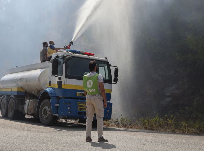 An Oxfam staff member stands near Civil Defense vehicles as volunteers battle wildfires in Qastal Ma'af, rural Latakia.