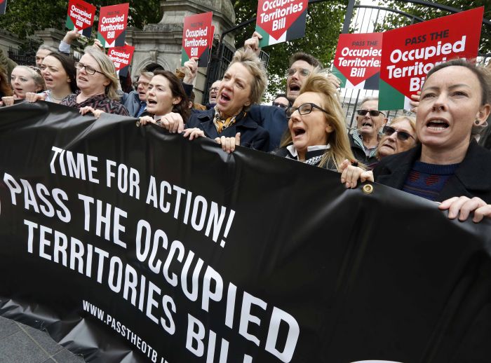 Protest group outside a government building holding a banner and signs calling to pass the Occupied Territories Bill.