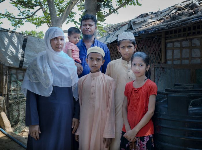Dil and her family of five standing in front of a makeshift hut in Cox Bazar