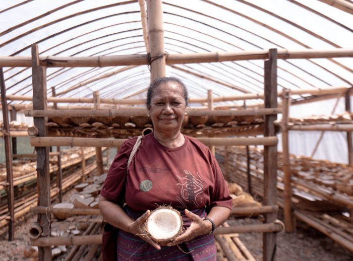 A lady holds a coconut towards the camera in a solar dryer house