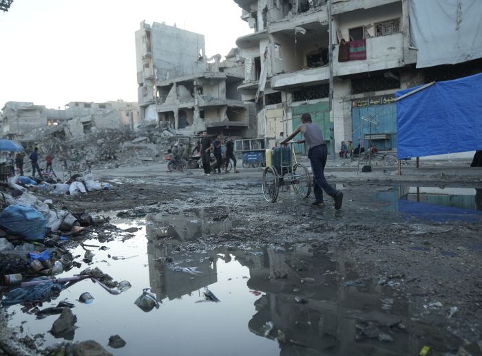 Destroyed buildings in Gaza. A man is pushing a cart with jerry cans on the top among the rubble