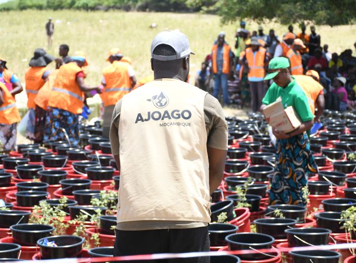 A man stands with his back to the camera, there are rows of buckets in front of him. People gather in the distance