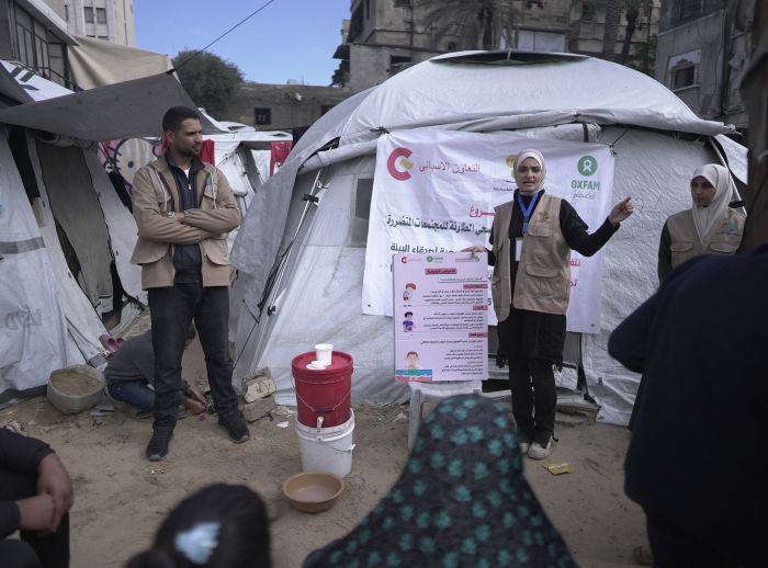 Oxfam partner health promoters leading a health promotion session. They are standing in front of white tents with red buckets