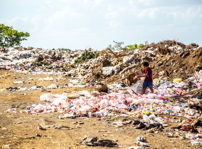 Boy walks through trash plastic waste landfill