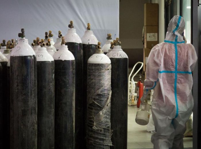 person in hazmat suit beside oxygen cylinders 
