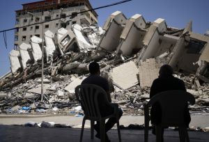 People sit in front of the destroyed Hanada building