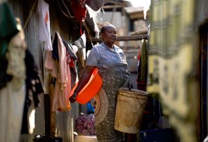 Woman standing between rows of hanging clothes with buckets in her hands in Narobi