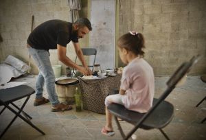 A dad preparing food from an Oxfam food parcel for his kid in Gaza. Up to 21,000 people are dying each day from conflict-fuelled hunger around the world