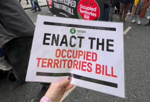 Person holding a poster with "Enact the Occupied territories bill" and the Oxfam Ireland logo during the nationwide demonstration