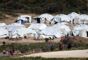 Asylum seekers stand next to tents near the sea at the Mavrovouni camp on Lesbos
