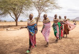 Five ladies in traditional attire walk across a dry, open landscape in Ongeli Village, Marsabit, heading to a participatory training under the DFAT-funded CLTS project by SND.