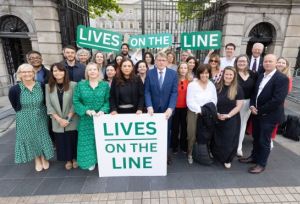 Group standing front of political building with banner "lives On The Lines"