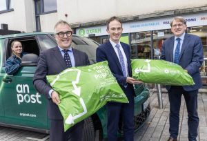 Minister Alan Dillon, with staff of An Post and Oxfam, standing beside an An Post van, holding PostBack bags at the official launch of PostBack