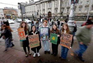 Students stand outside Trinity College Dublin holding signs calling for climate action.