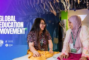 Two women speaking to each other while holding clothes on a table
