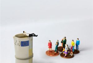 Miniature character setup with man in suit relaxing on top of a pile of 200 euro bills and a group of ordinary people standing on cents