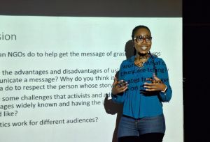 Female speaker in front of a projection of a presentation