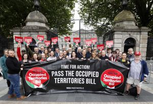 Protest group outside a government building holding a banner and signs calling to pass the Occupied Territories Bill.