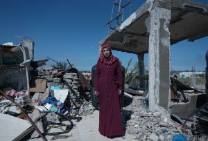 A woman wearing a red hijab stands among the rubble of a destroyed home. She is showing signs of pregnancy in Gaza.