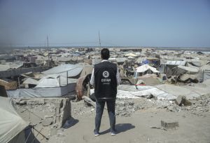 Osama, Oxfam Staff, walks among tents and rubble in Gaza City