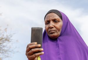 Ebla Hussein Ahmed reading a message from her mobile phone at her home in Elben, Wajir County, Kenya. She receives her monthly cash payment notification via her phone.