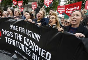 Protest group outside a government building holding a banner and signs calling to pass the Occupied Territories Bill.