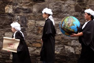 Young climate judges holding a scroll saying 'verdict: guilty' and giant globe while wearing robes and wigs.