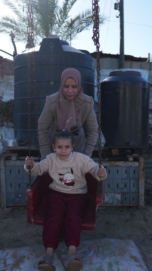 Hiba plays with her daughter at a swing outdoors