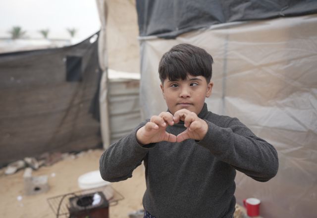 Image of a kid in a camp in Gaza forming a heart with his hand.