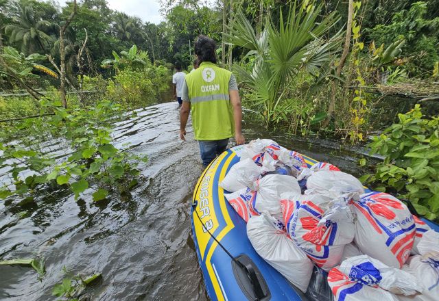 Oxfam staff pull a supply-laden inflatable boat through a flooded area surrounded by greenery.