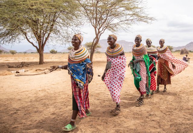 Five ladies in traditional attire walk across a dry, open landscape in Ongeli Village, Marsabit, heading to a participatory training under the DFAT-funded CLTS project by SND.